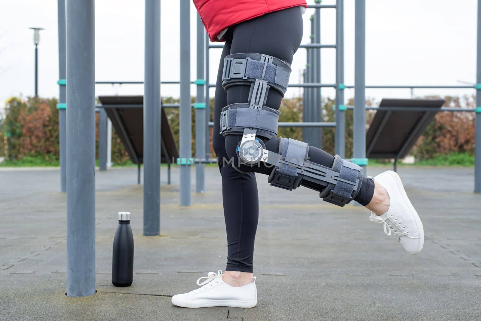 Woman wearing sport clothes and knee brace or orthosis after leg surgery, walking in the park. Medical and healthcare concept.