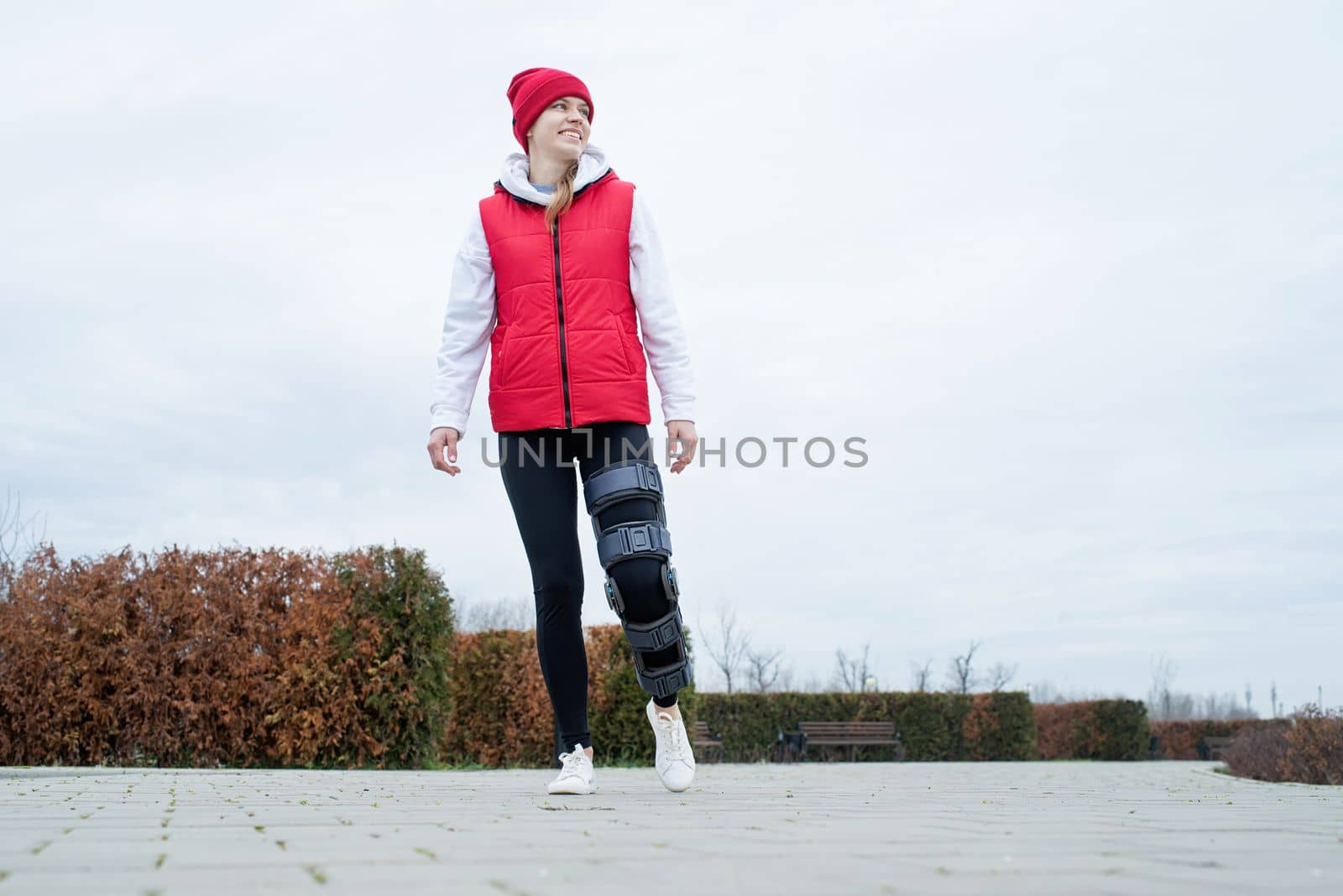 Woman wearing sport clothes and knee brace or orthosis after leg surgery walking in the park . Medical and healthcare concept.