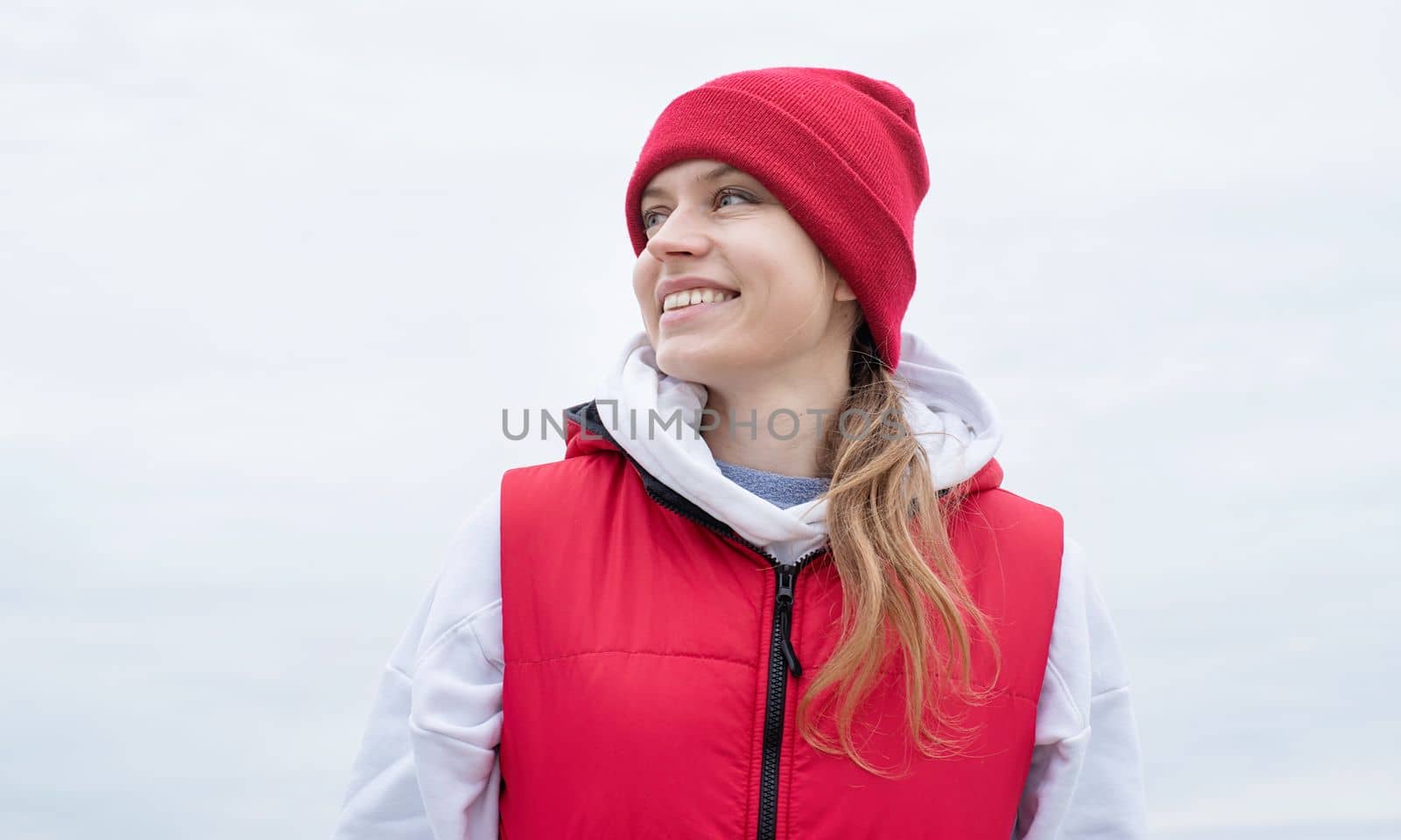 Beautiful happy caucasian woman wearing red and white sportive clothes walking outdoors in cloudy day
