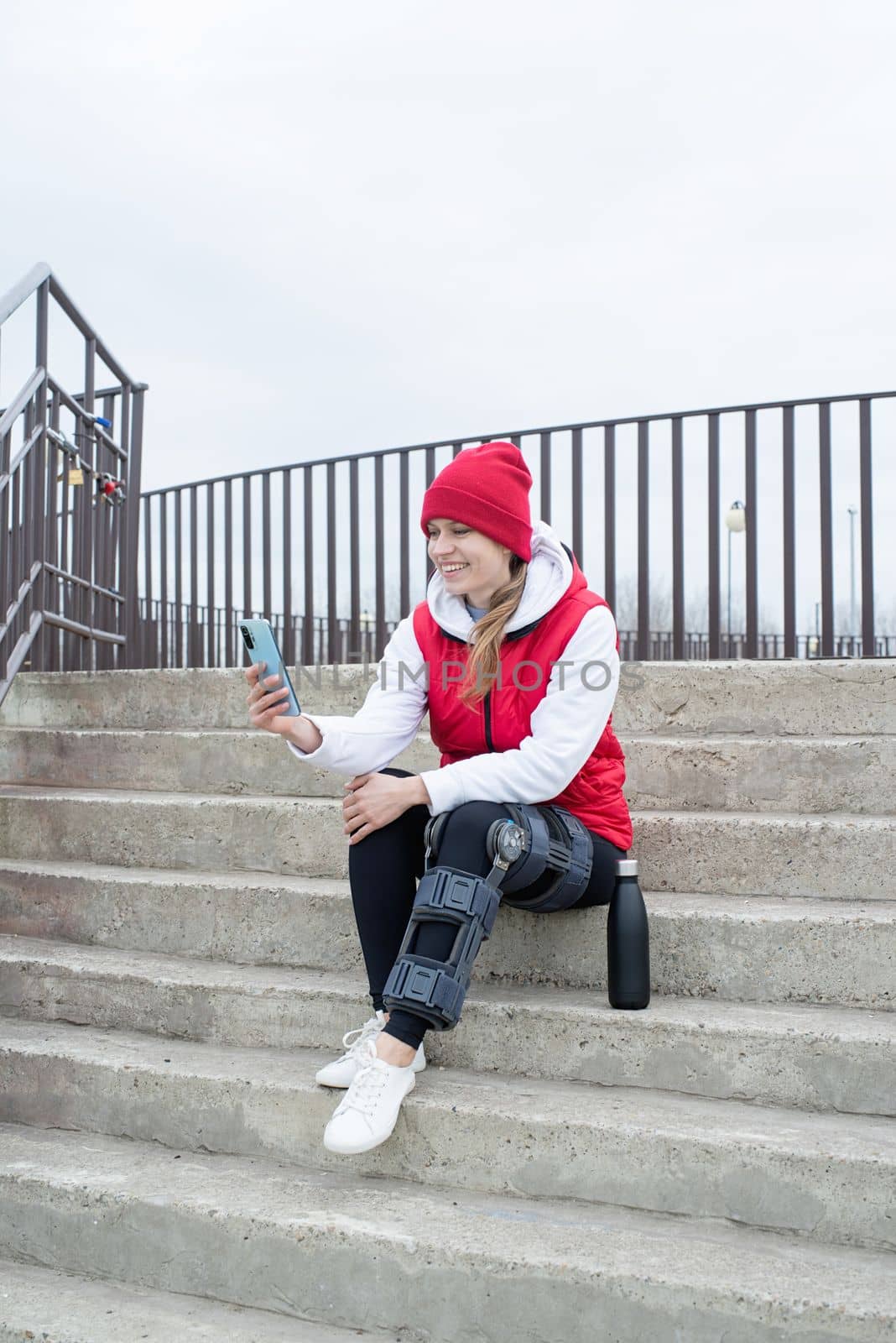 Woman wearing sport clothes and knee brace or orthosis after leg surgery, walking in the park. Medical and healthcare concept.