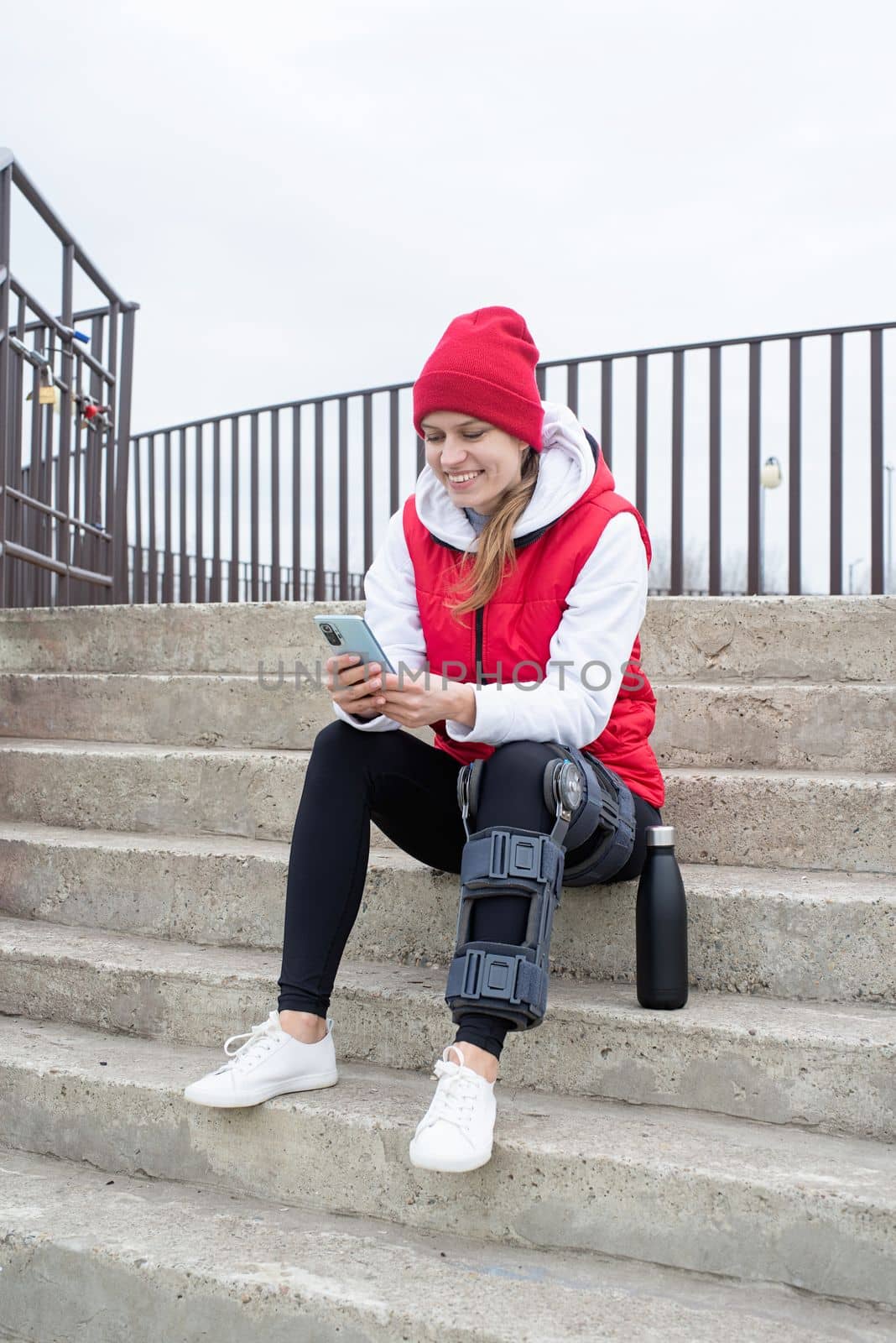 Woman wearing knee brace or orthosis after leg surgery, walking in the park by Desperada