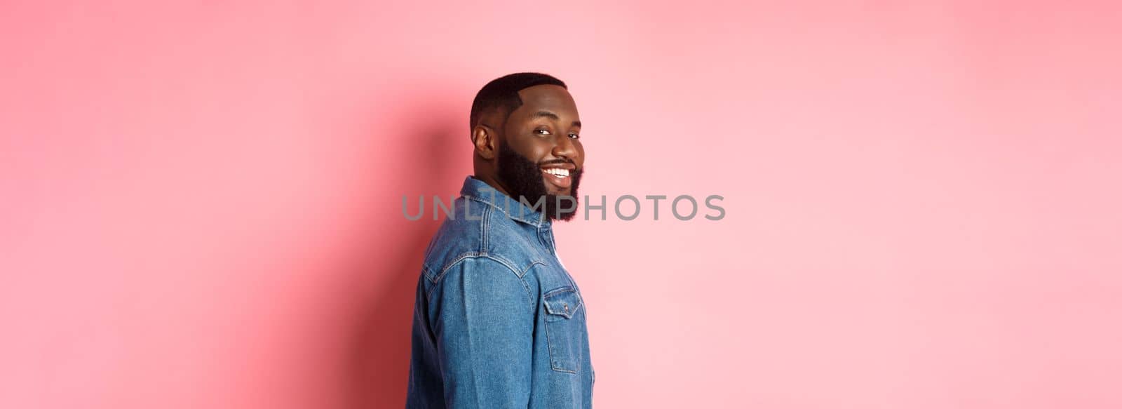 Handsome african-american man with beard, turn face at camera and smiling confident, standing over pink background by Benzoix