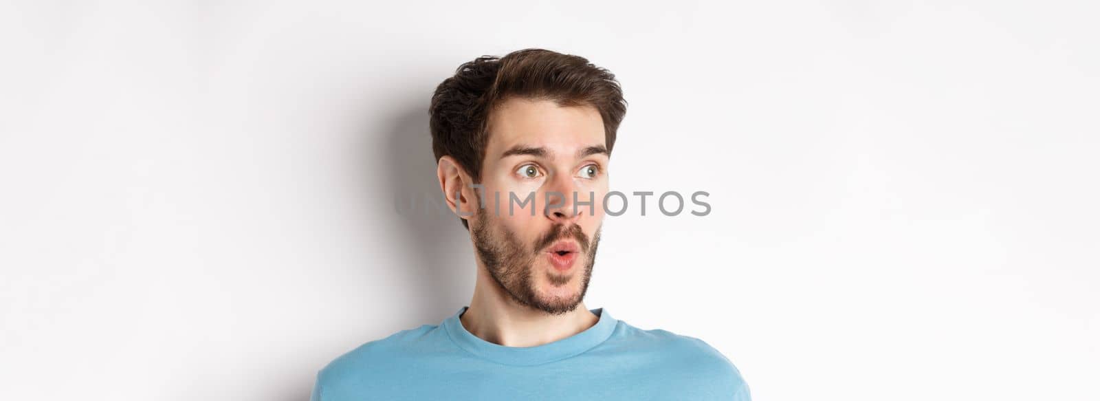 Close-up of impressed caucasian man saying wow, looking left amazed, checking out promotion deal, white background. Copy space