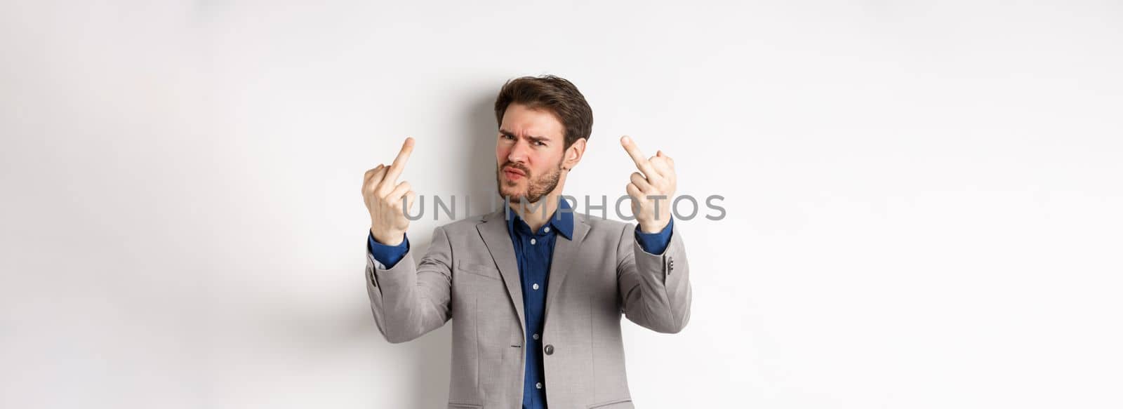 Rude businessman in suit showing middle finger, fuck you gesture, look annoyed and pissed-off, standing on white background.