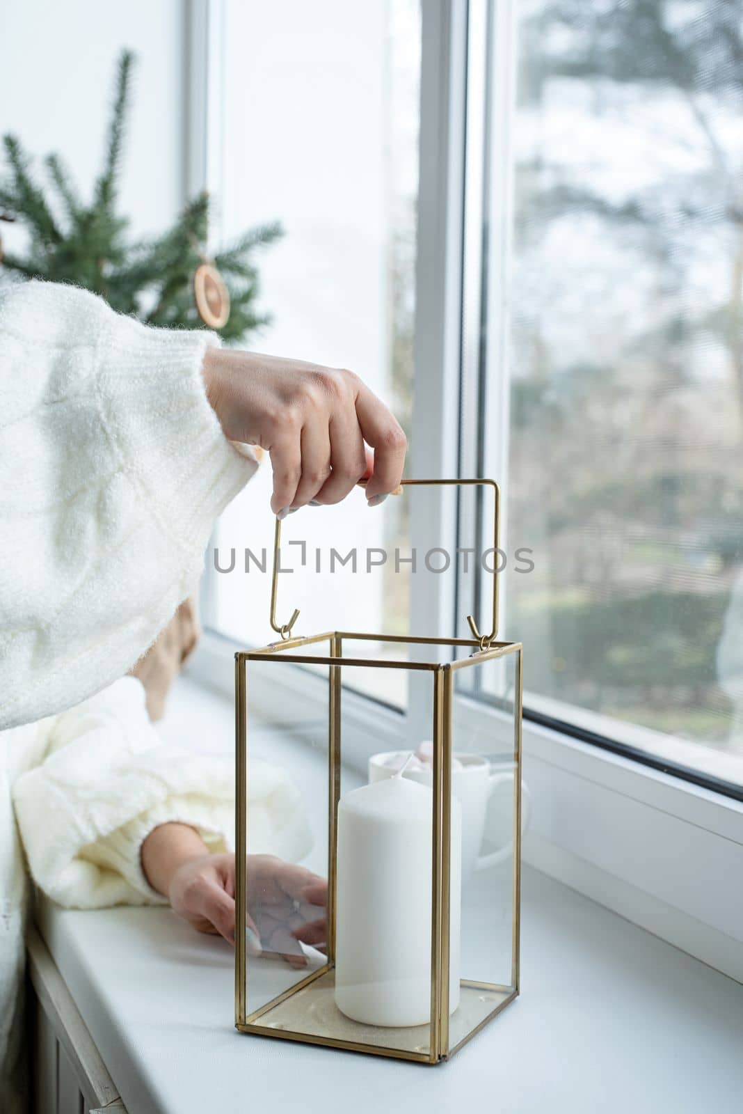 Woman hand in cozy sweater holding candle near window. Cozy autumn or winter, hygge lifestyle