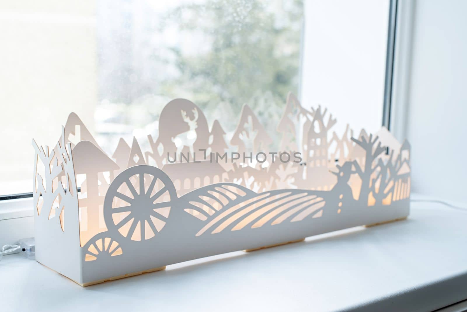 Beautiful white paper or plastic winter decoration with lights on windowsill by Desperada