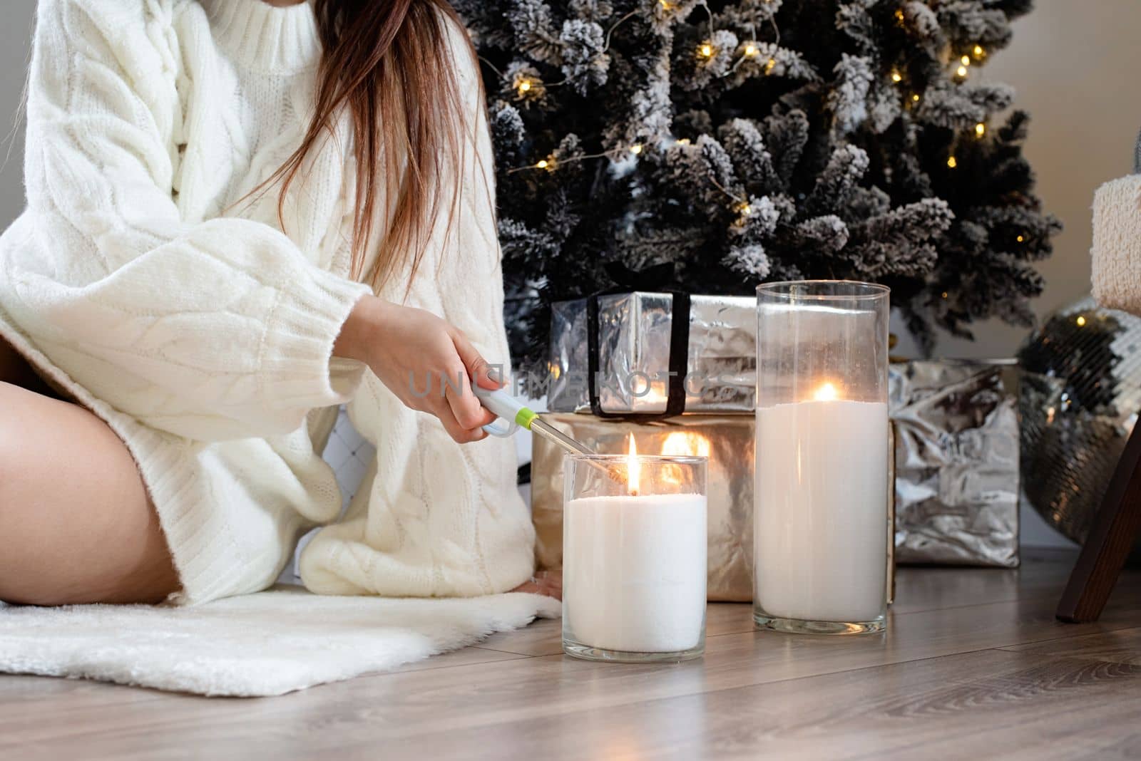 Merry Christmas and Happy New Year. Woman in warm white winter sweater sitting by christmas tree unpacking gifts