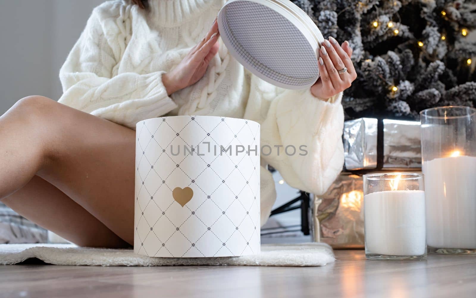 Woman in warm white winter sweater lying in bed at home at christmas eve holding cup with marshmallows, fir tree behind by Desperada