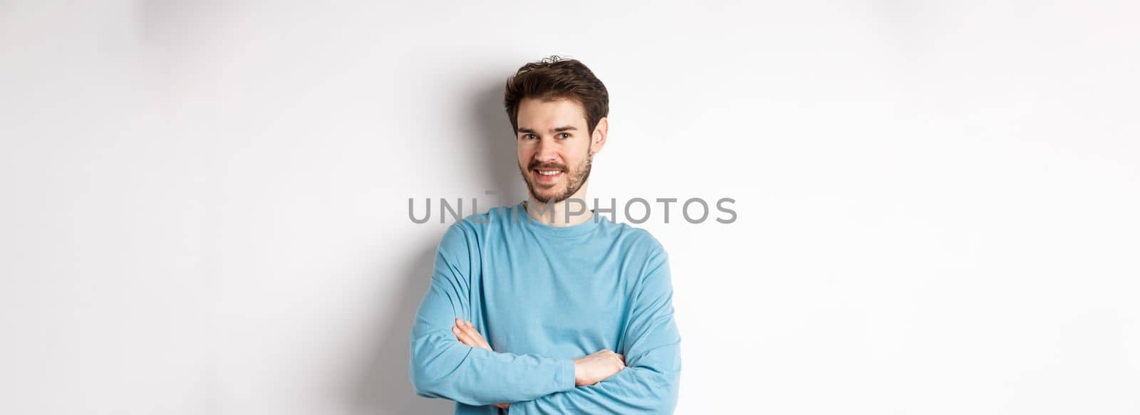Confident young man with beard, cross arms on chest and smile at camera, standing like professional over white background.