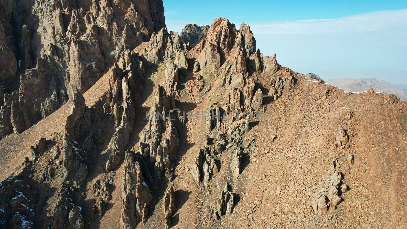 Top view of the high rocky mountains with trails. In places there is snow and yellow-orange plants grow. Shadows from clouds float on the rocks. A place to climb to the top. The mountains of Almaty