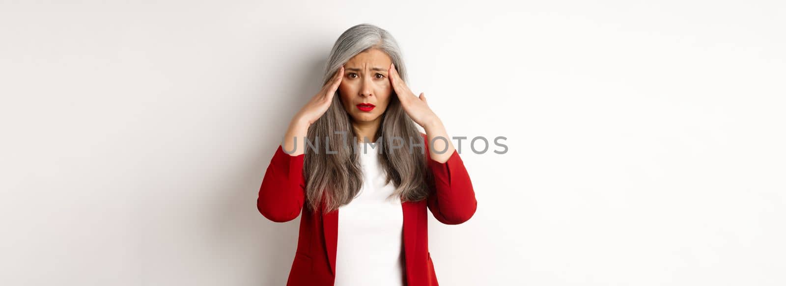 Troubled asian female entrepreneur having headache, touching head and frowning, standing over white background.
