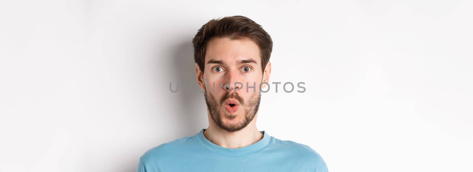 Close-up of surprised man face, saying wow and staring at camera amazed, standing on white background by Benzoix