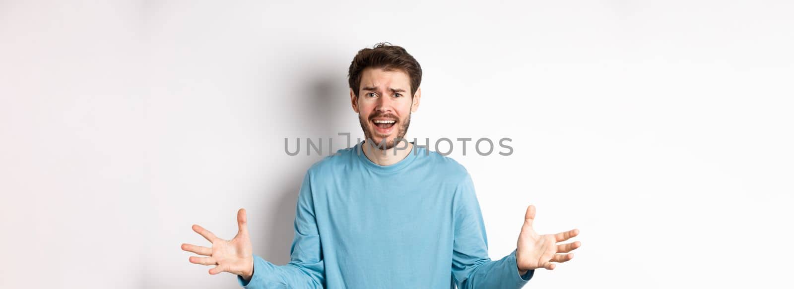 Image of frustrated and worried young man shaking hands, trying to explain something, standing anxious against white background.