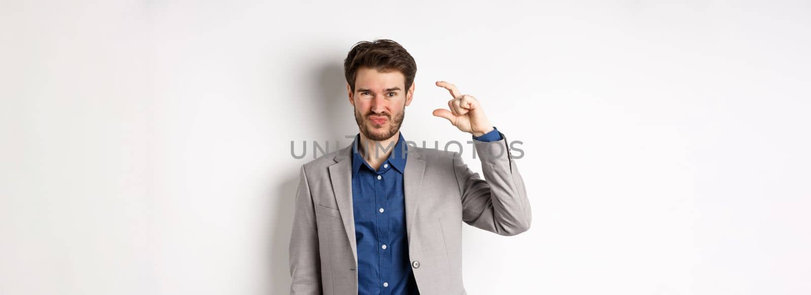 Disappointed businessman showing small size and grimacing upset, little income, standing displeased against white background.