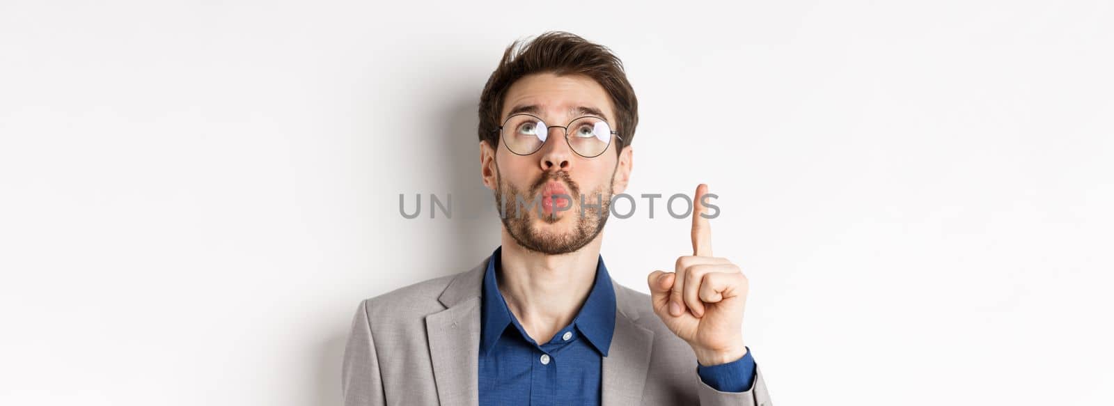 Excited handsome man in glasses and business suit, look up and pointing at top advertisement, exclaim wow with amazed expression, white background by Benzoix