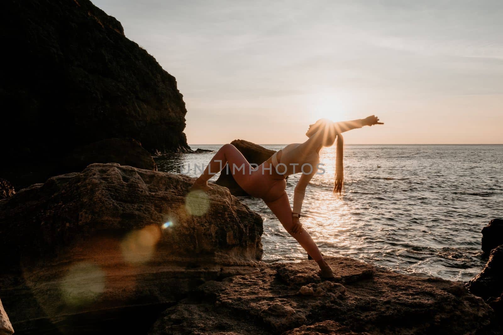 Young woman with black hair, fitness instructor in pink sports leggings and tops, doing pilates on yoga mat with magic pilates ring by the sea on the beach. Female fitness daily yoga concept