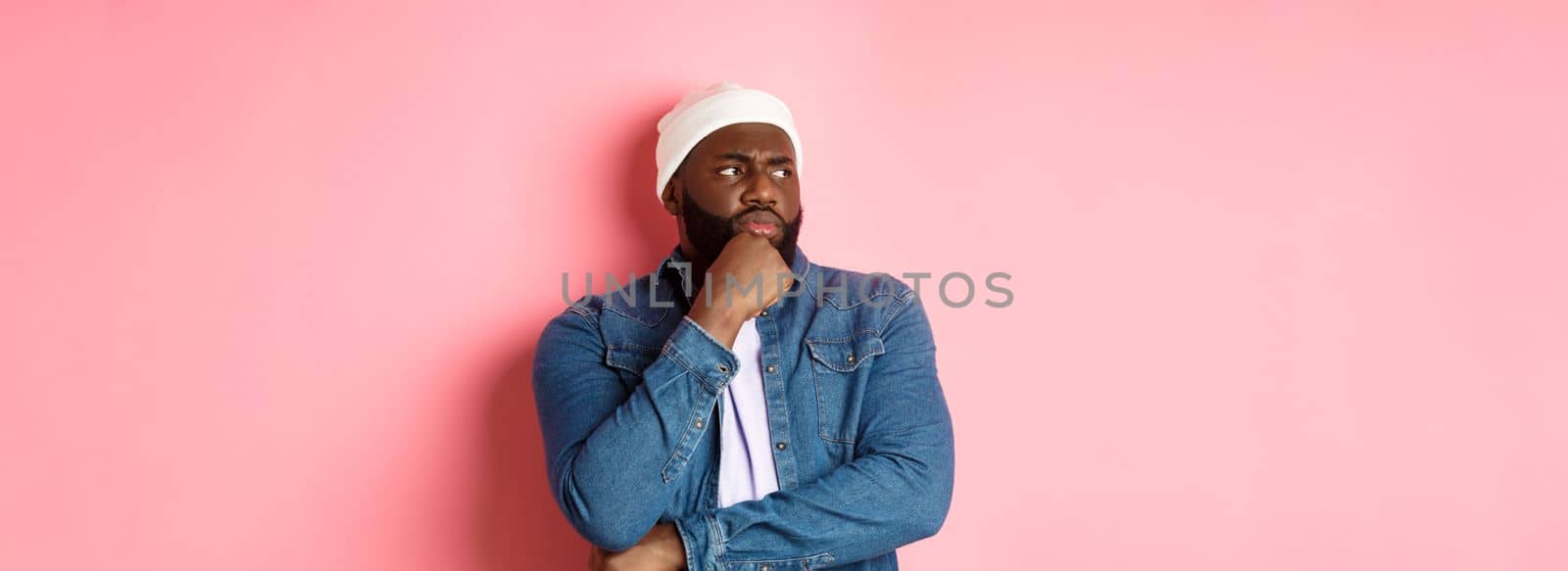 Serious thoughtful african american male model making decision, looking left concerned, thinking or having doubts, standing over pink background by Benzoix