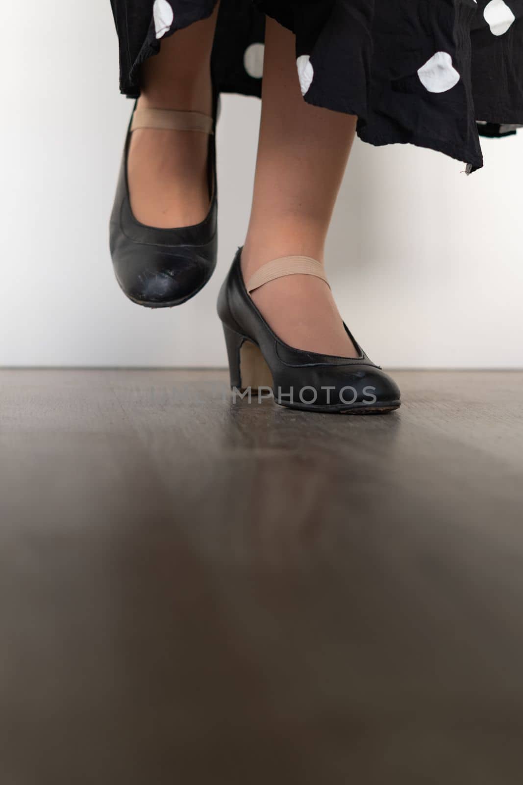 legs of woman dancing flamenco with black clothes on wooden floor and white background