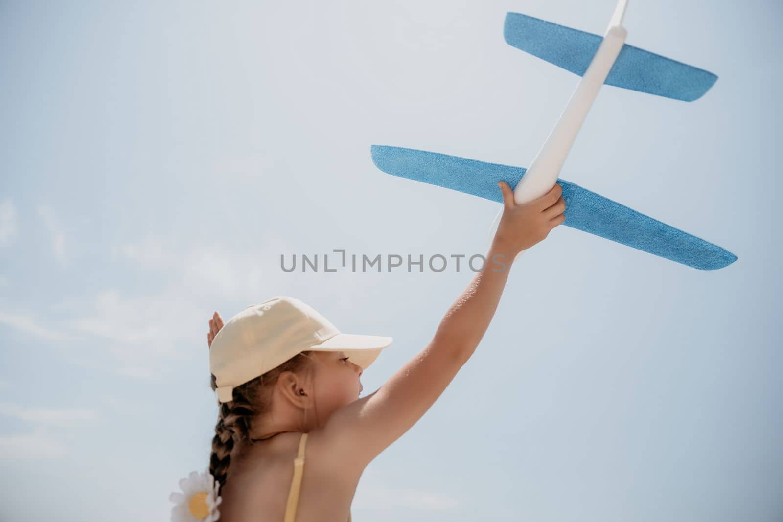 Kid playing with toy airplane. Children dream of travel by plane. Happy child girl has fun in summer vacation by sea and mountains. Outdoors activities at background of blue sky. Lifestyle moment