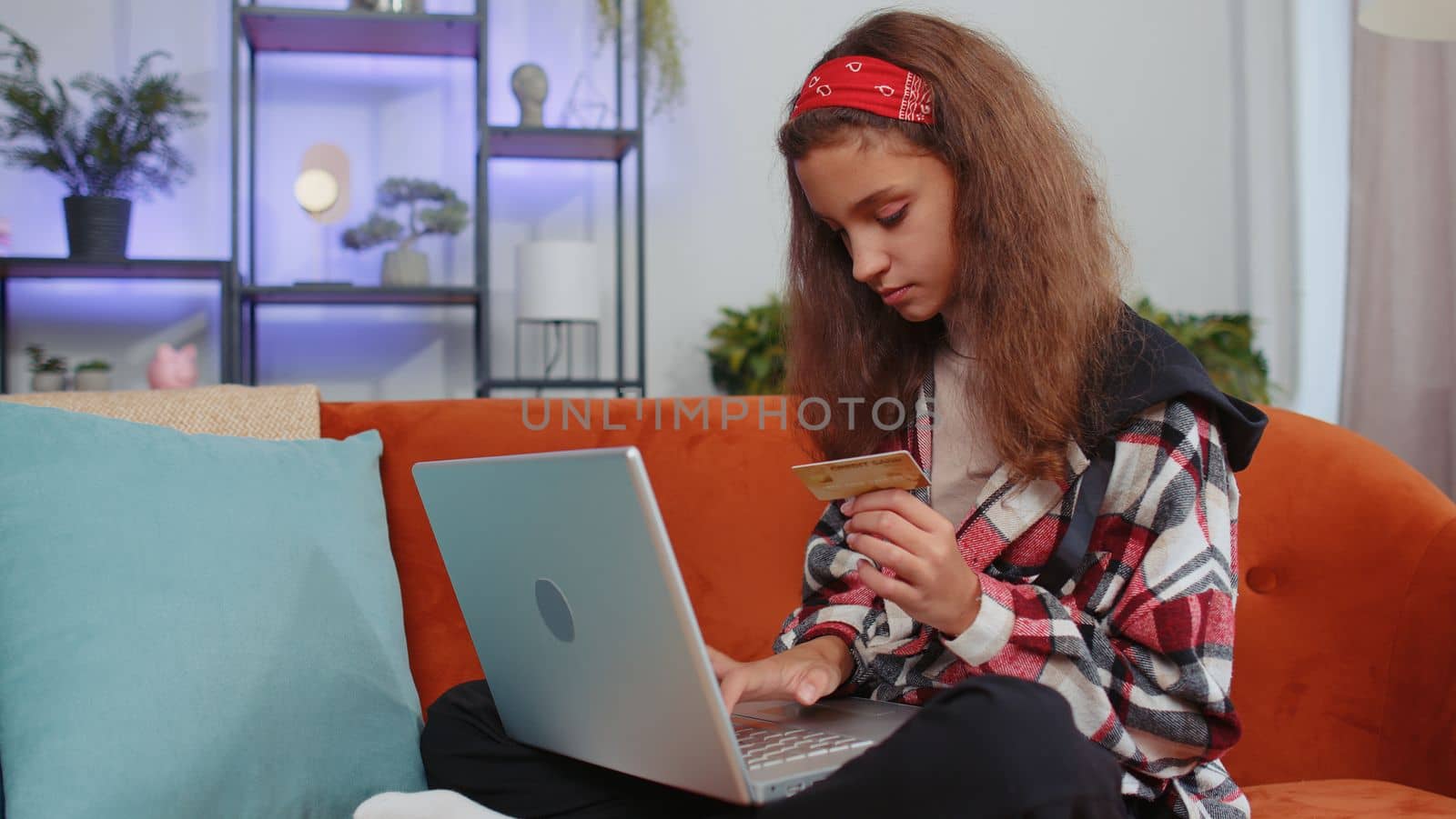 Portrait of preteen girl using credit bank card and laptop computer while transferring money, purchases online shopping, order food delivery at home. Young teenager child, kid on couch at home room