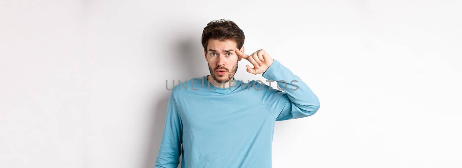 Annoyed caucasian man roll finger on temple, are you stupid or crazy gesture, scolding someone acting strange, standing in sweatshirt over white background.