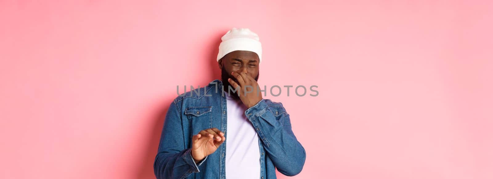 Disgusted black man shut nose and cringe from awful smell, showing refusal gesture, standing over pink background by Benzoix
