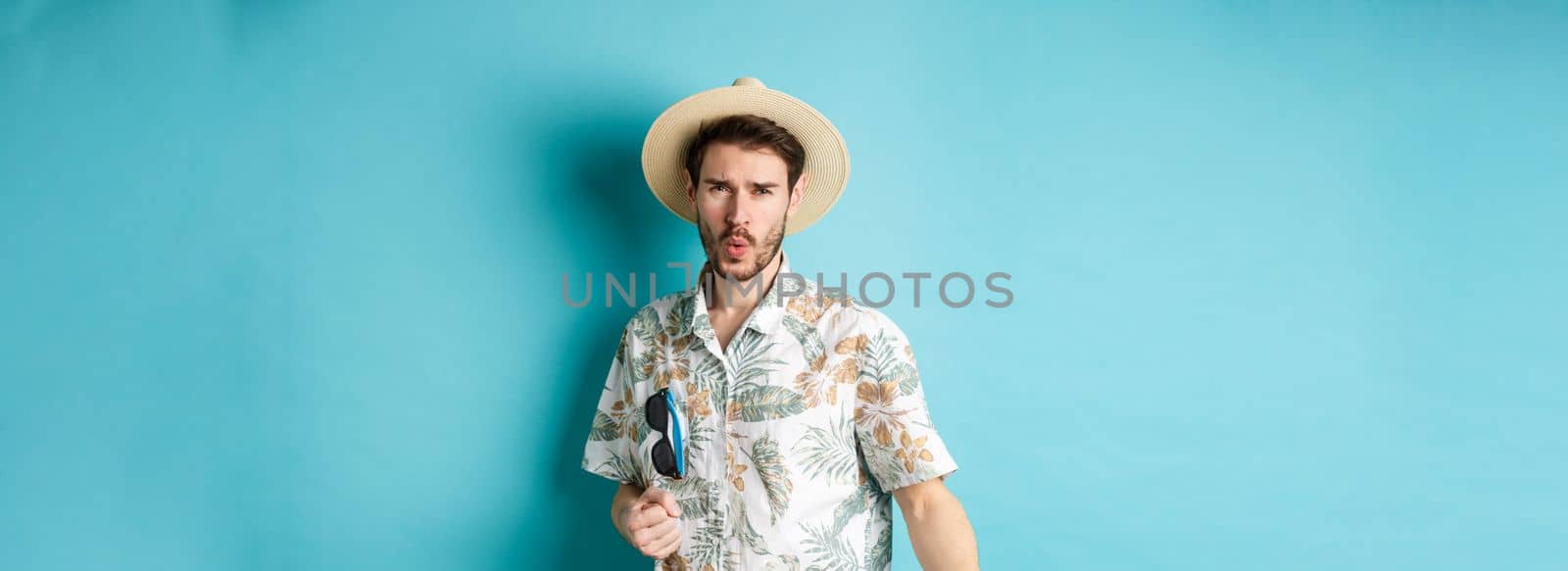 Happy tourist in hawaiian shirt and summer hat dancing, having fun on vacation, standing on blue background.