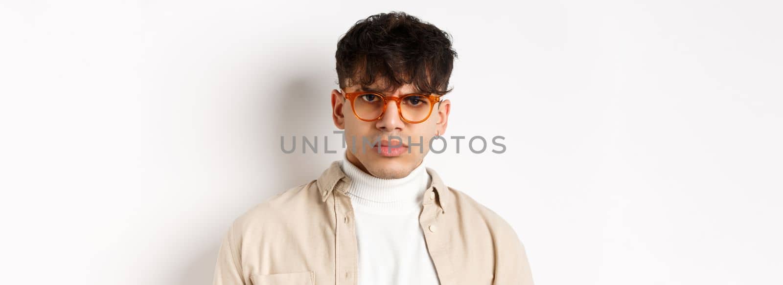 Close up portrait of angry frowning guy looking with dispise, standing mad on white background, wearing glasses.