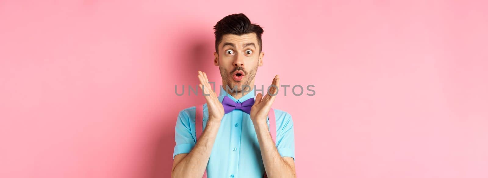 Portrait of funny guy say wow, staring amazed at camera, checking out awesome offer, standing in classy bow-tie on pink background.