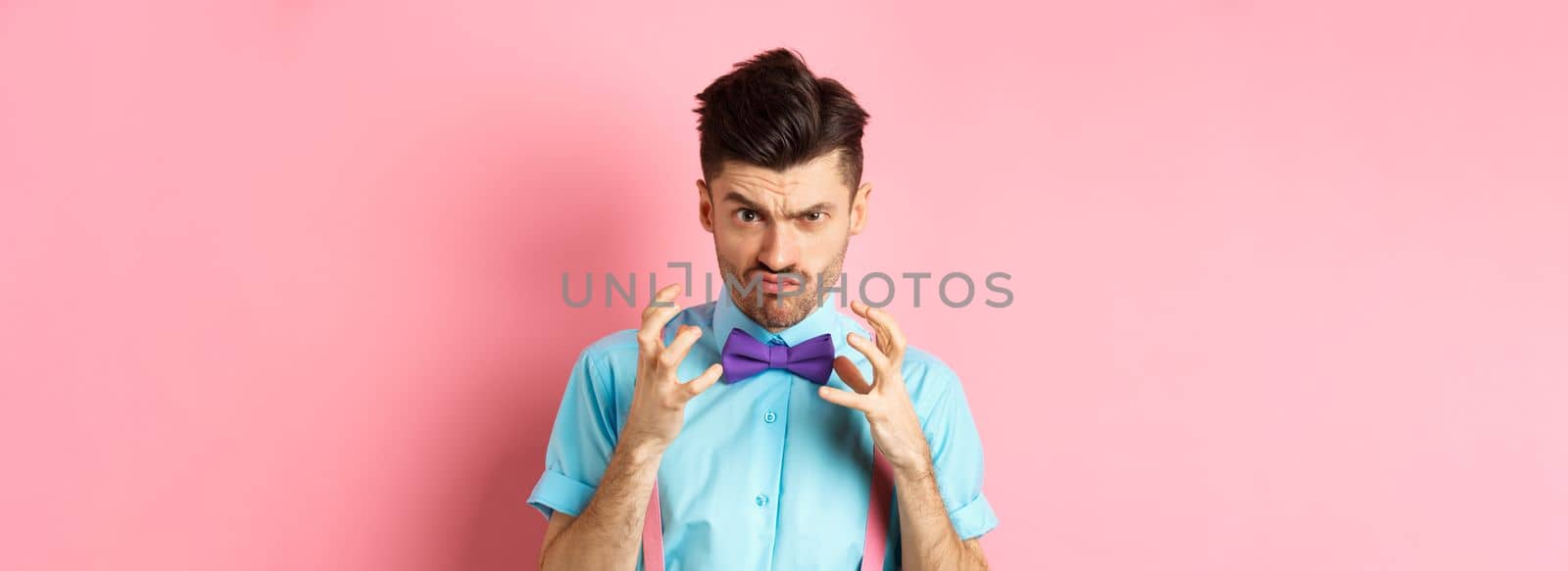 Image of angry guy in bow-tie gonna strangle someone, raising hands up and looking mad or pissed-off, feeling furious, standing on pink background.