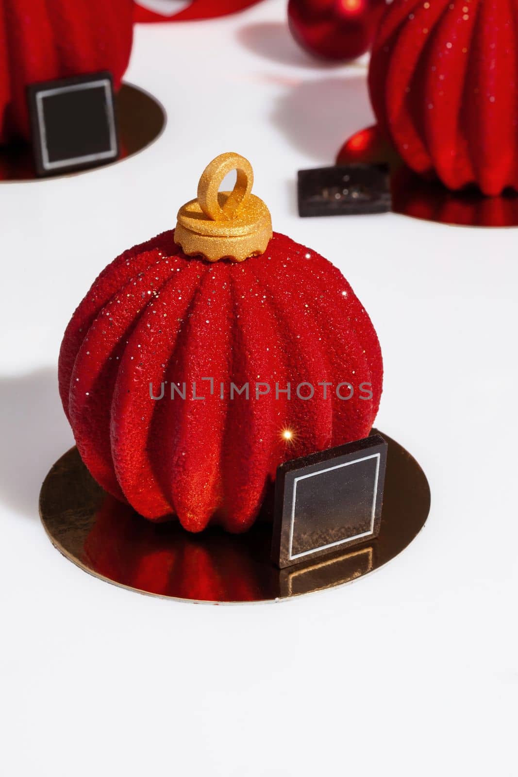 Christmas ball shaped pastries covered with scabrous sparkling red sugar icing with chocolate on golden serving cardboard on white background. Creating festive mood and atmosphere with sweets