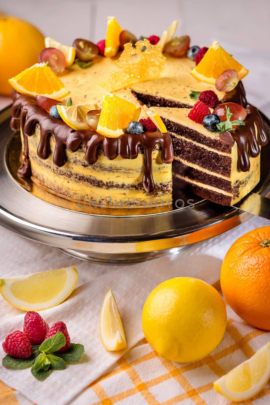 Delicious chocolate sponge cake with citrus custard cream decorated with ganache, slices of fresh oranges, lemon and ripe berries on cake stand