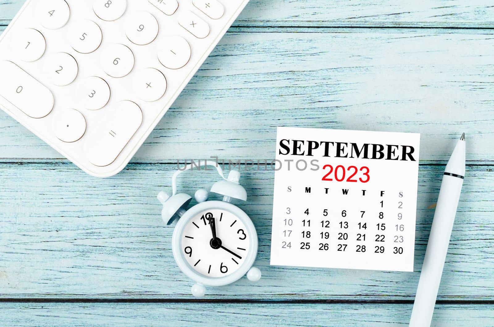 September 2023 Monthly calendar year and alarm clock with calculator on blue wooden background.