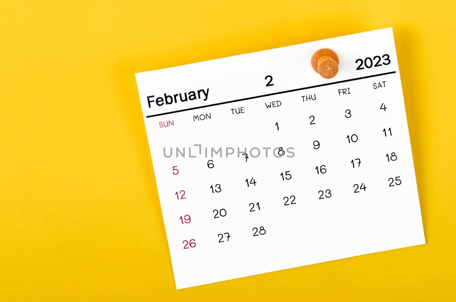 February 2023 monthly calendar and wooden push pin on yellow background.
