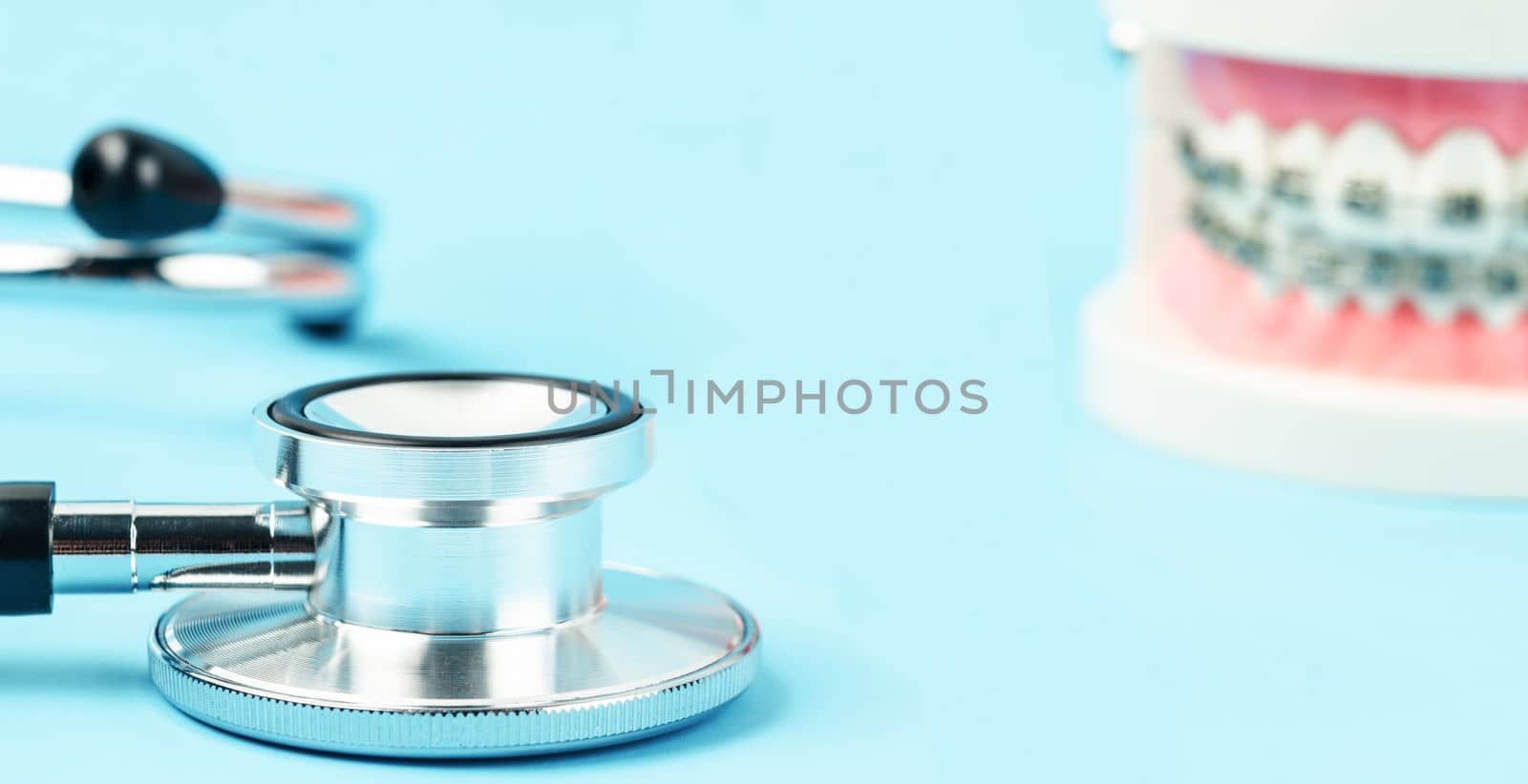 Medicine equipment stethoscope and metal wire dental braces on model teeth on blue background. Health dental care concept.