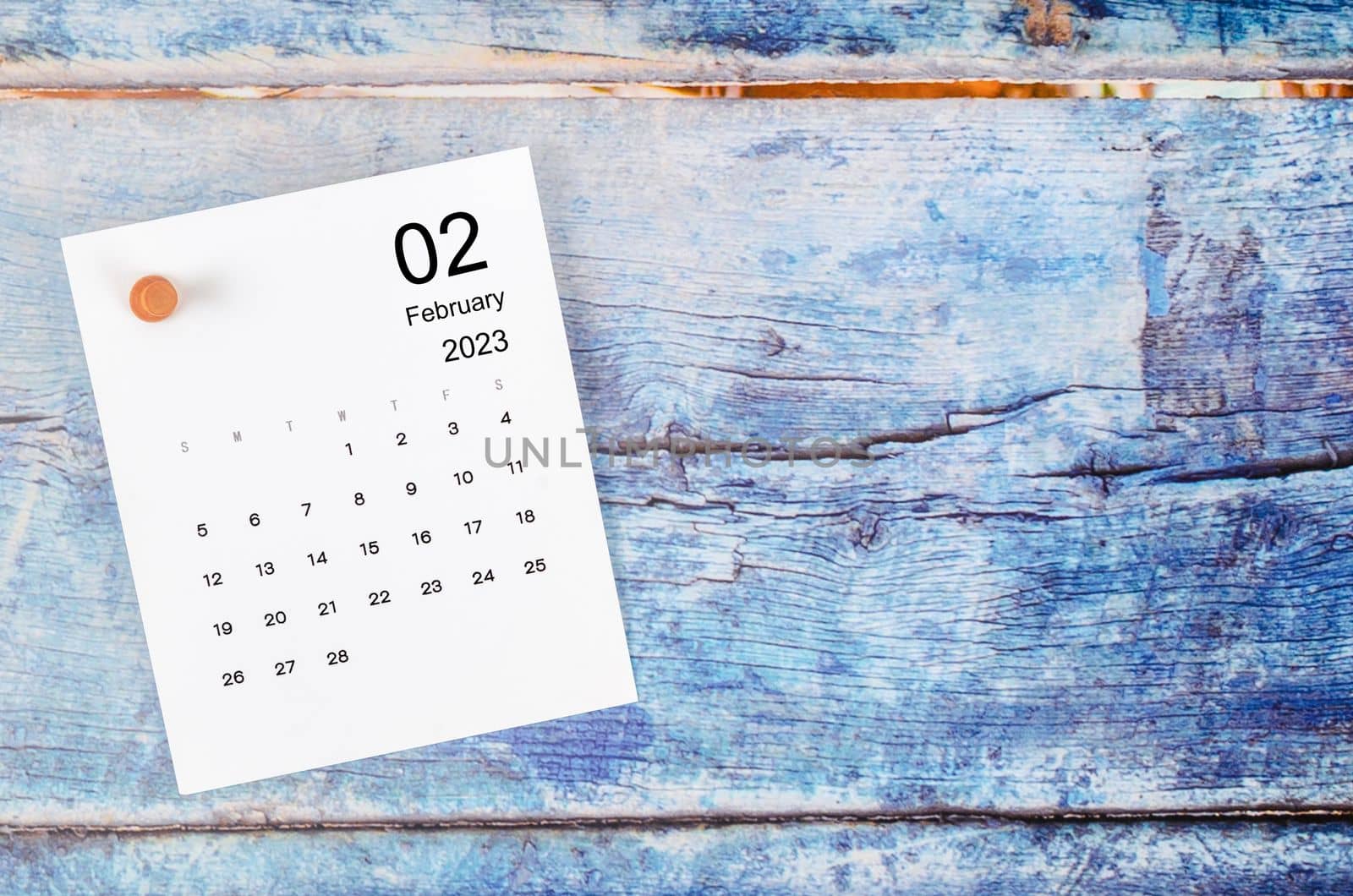 February 2023 monthly calendar and wooden push pin on blue wooden background.