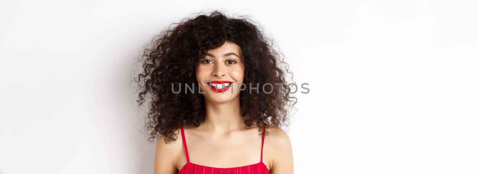 Close-up of beautiful woman with curly hairstyle, wearing red dress and lipstick, smiling happy at camera, white background by Benzoix