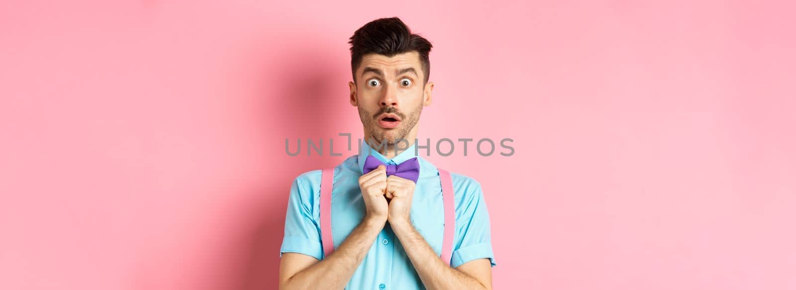 Startled and worried classy man in moustache, gasping and holding breath shocked, standing oin bow-tie over pink background.