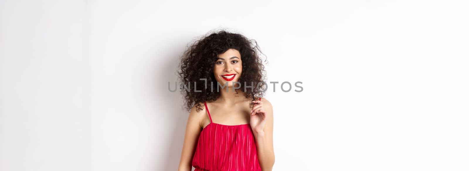 Beautiful woman with curly hair and makeup, wearing elegant dress for romantic date, standing happy on white background by Benzoix