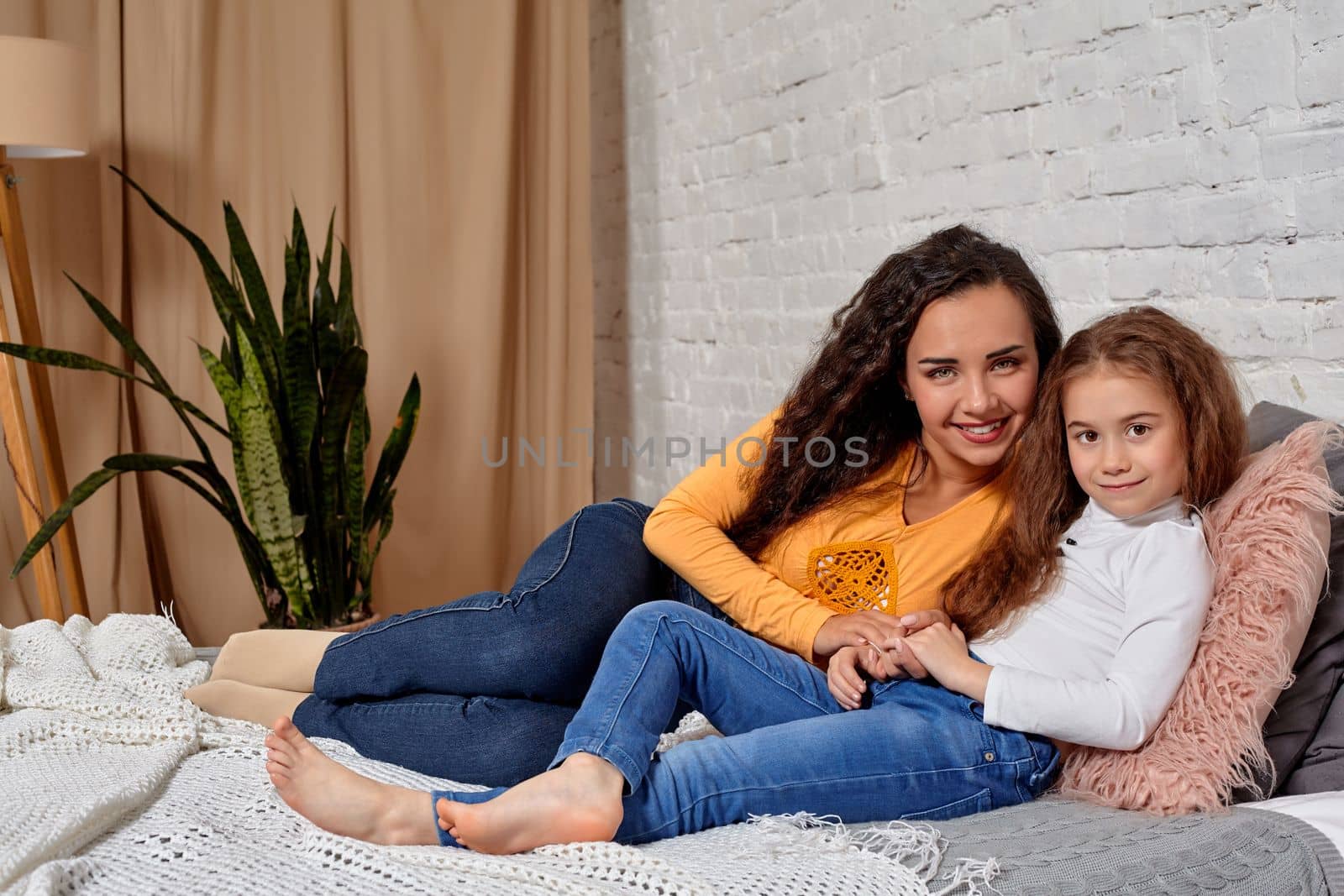 Love of young mother and daughter. They lie on the bed at home and have fun, they feel good.