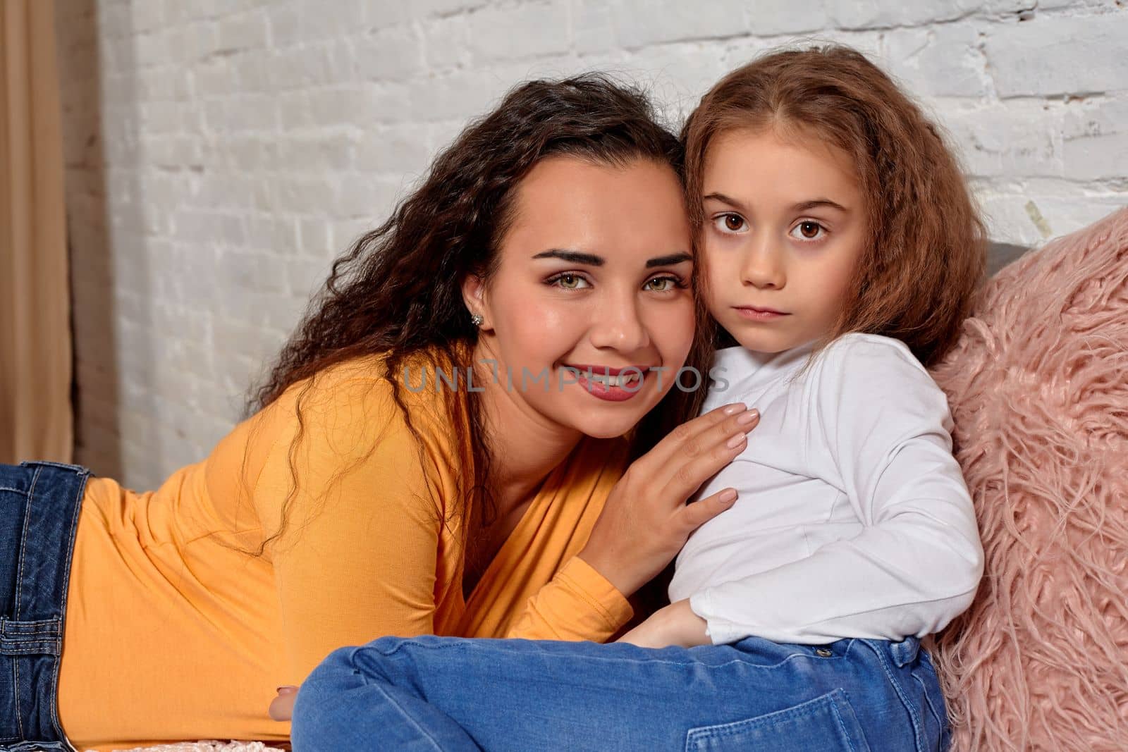 Love of young mother and daughter. They lie on the bed at home and have fun, they feel good.