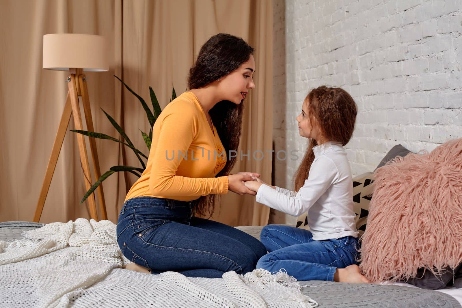 Love of young mother and daughter. They sit on the bed at home and have fun, they hold each other and show their emotions