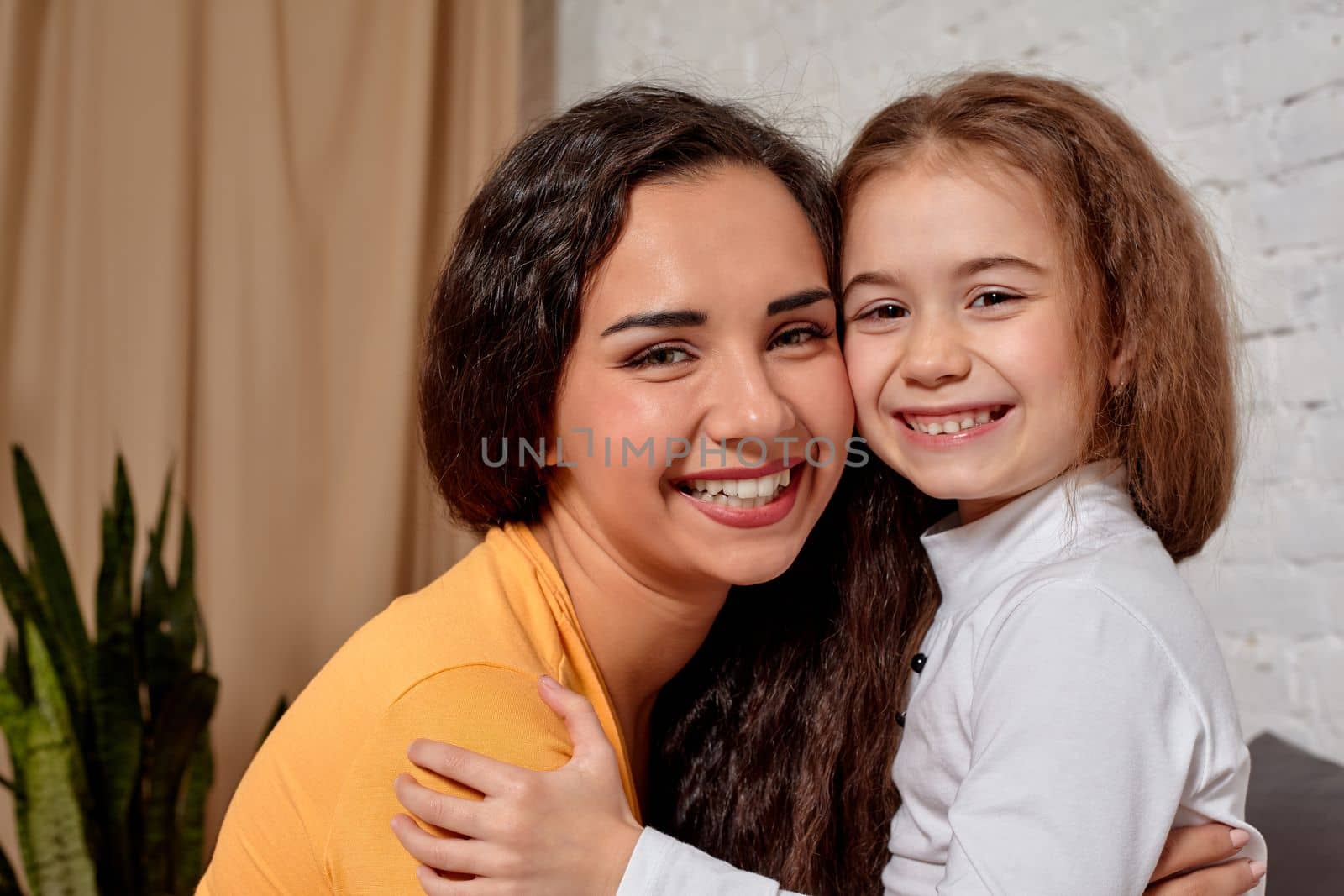 Love of young mother and daughter. They sit on the bed at home and have fun, they hold each other and show their emotions