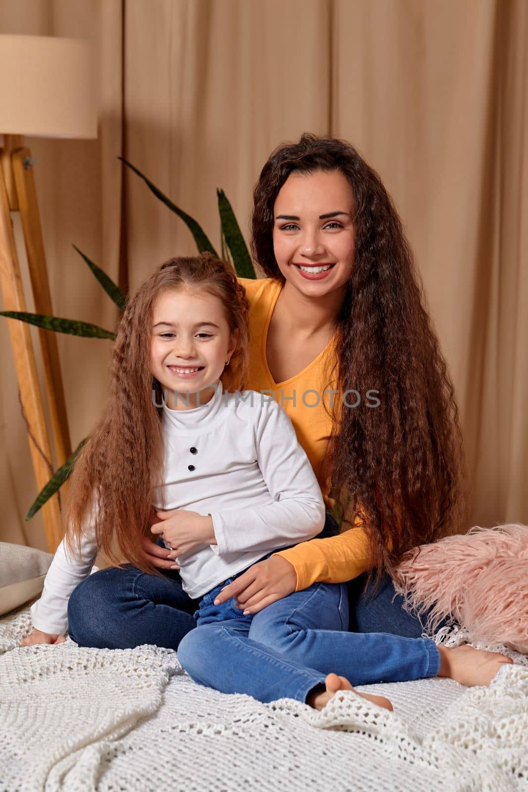 Love of young mother and daughter. They sit on the bed at home and have fun, mother hugs daughter