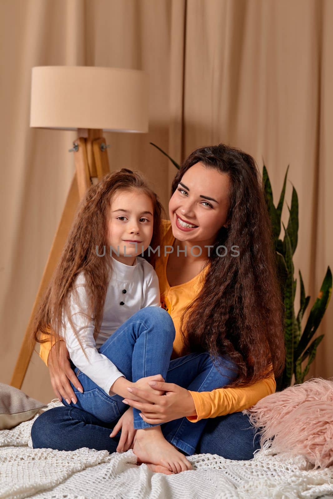 Love of young mother and daughter. They sit on the bed at home and have fun, mother hugs daughter