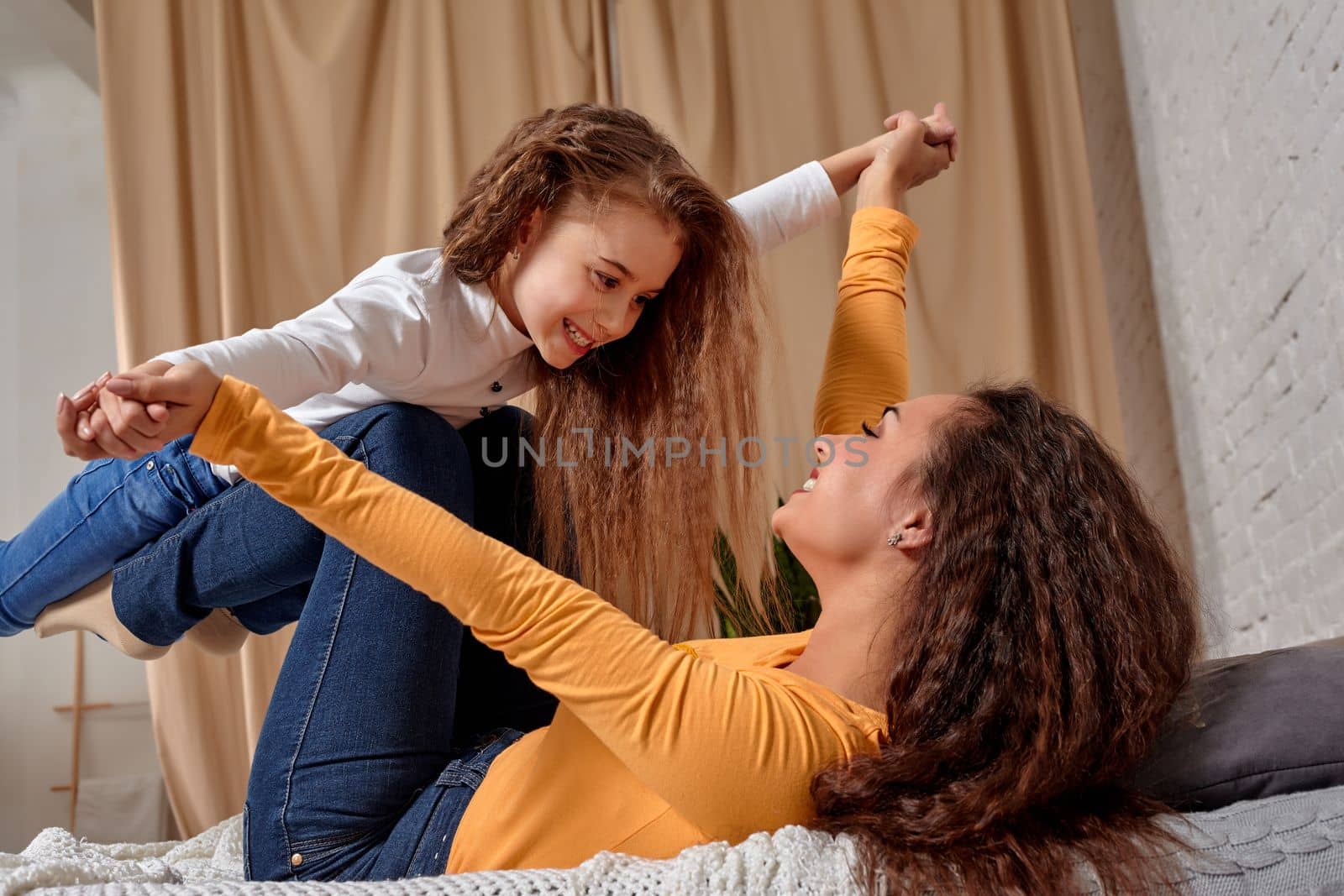 Love of young mother and daughter. They lie on the bed at home and have fun by nazarovsergey