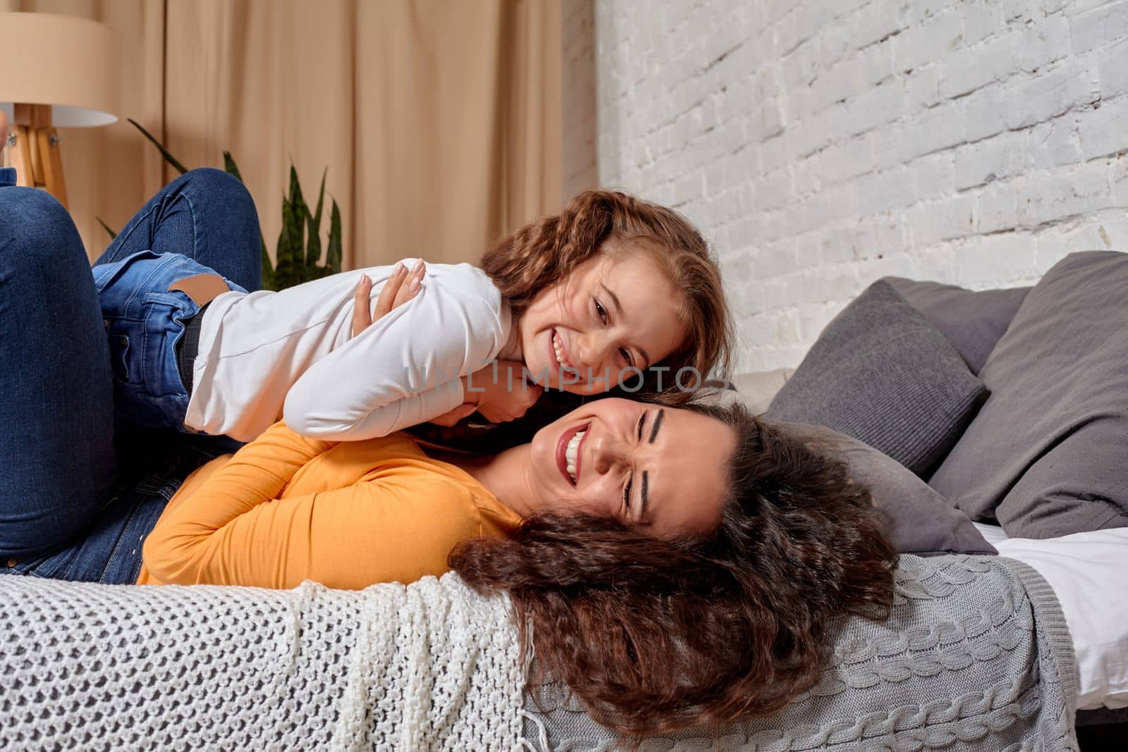 Love of young mother and daughter. They lie on the bed at home and have fun by nazarovsergey