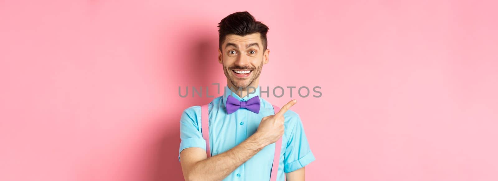 Portrait of handsome happy man showing logo, pointing left and smiling at camera, recommending shop offer, standing on pink background by Benzoix