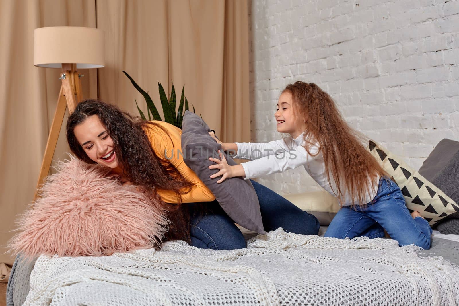 Young mom and daughter fooling around with pillow fights on the bed by nazarovsergey