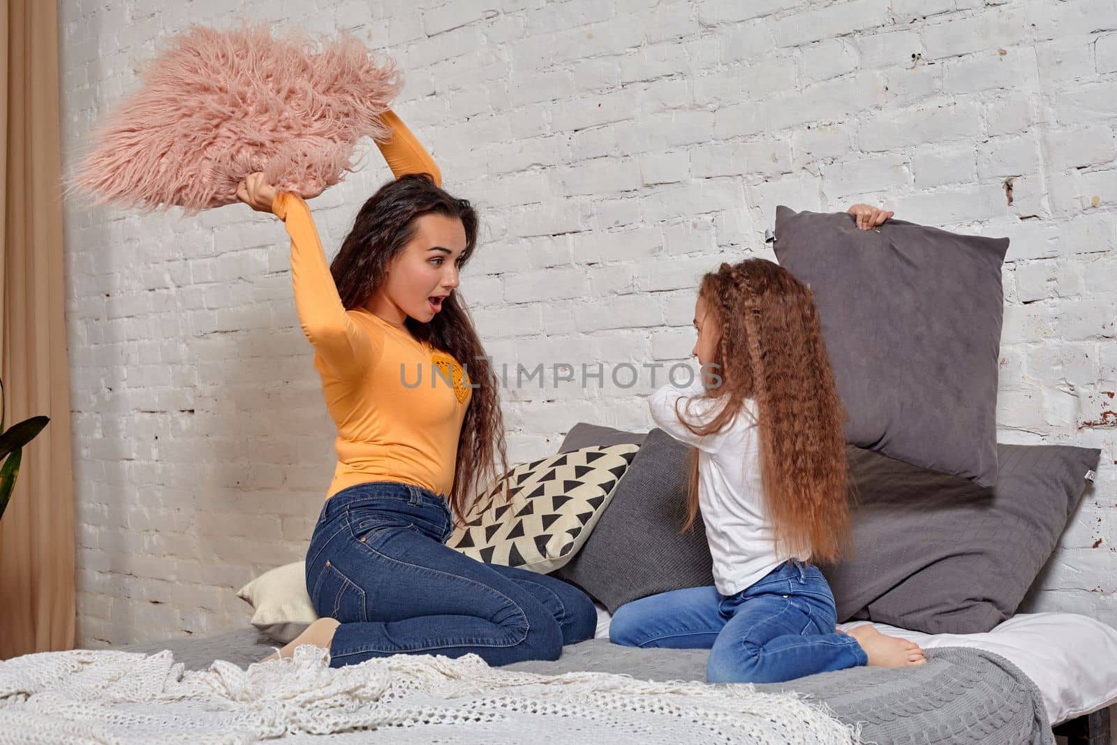 Young mom and daughter fooling around with pillow fights on the bed by nazarovsergey
